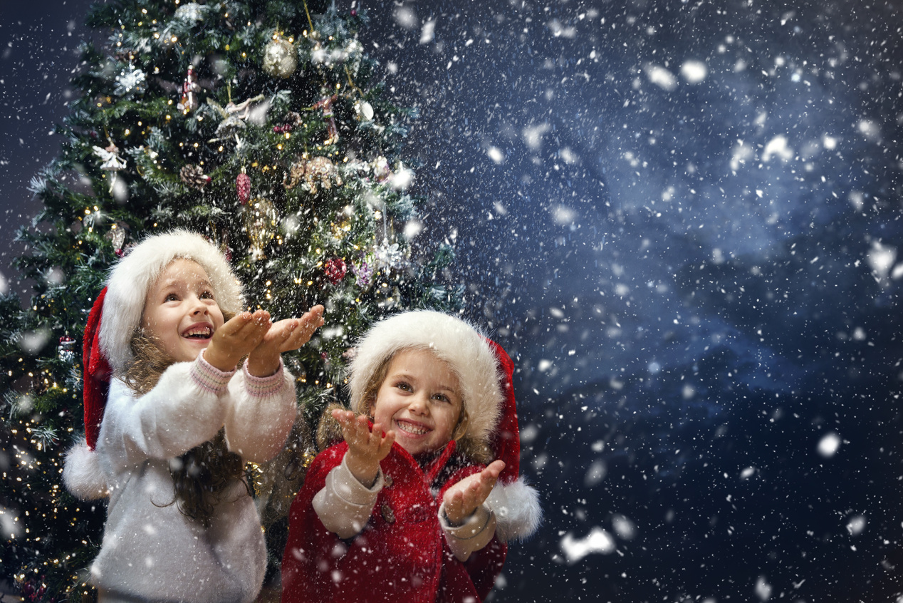 Christmas funny Kids catching Snow in Hands. Happy Children on Winter Holiday Vacation playing outside. Snowfall. Xmas Eve Night